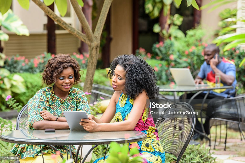 Young African businesswomen using digital tablet Two attractive Nigerian women sitting in cafe with tablet. Female business colleagues working remotely, Nigeria, Africa. Nigeria Stock Photo