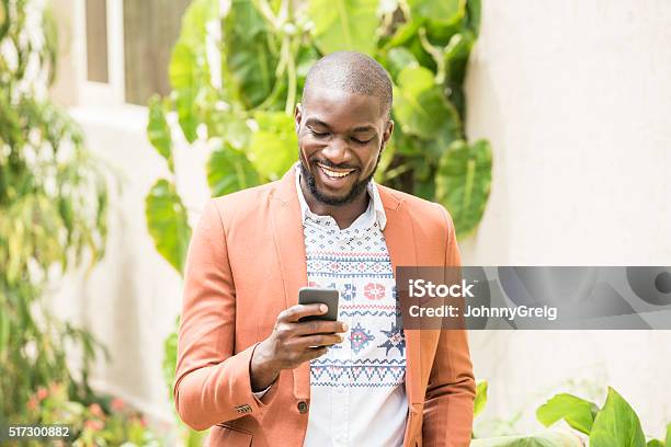 Candid Portrait Of Nigerian Man Using Cell Phone Smiling Stock Photo - Download Image Now