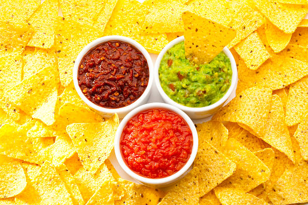 Three bowls with pico de gallo, mexican salsa and salsa guacamole with nachos around the bowls shot from above. Predominant colors are red and yellow. DSRL Studio photo taken with Canon EOS 5D Mark II and EF100mm f/2.8L Macro IS USM Lens