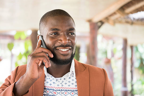 junge afrikanische mann am handy, wegsehen lächeln - nigerian culture men africa african culture stock-fotos und bilder