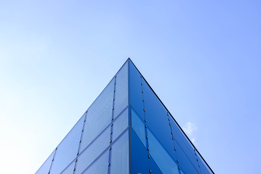 Upward view of a triangular building facade with blue sky and blue reflected in the windows