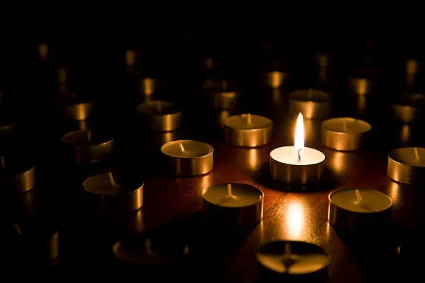 Single lit tealight candle surrounded by new unlit tealight candles that have never been burned