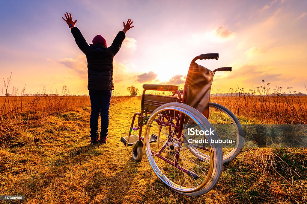 Miracle recovery: young girl gets up from wheelchair and raises Miracle recovery: young girl gets up from wheelchair and raises hands up. Overjoyed young girl  standing up from a wheelchair outdoors. Shot in meadow. Recovery concept Miracle Stock Photo