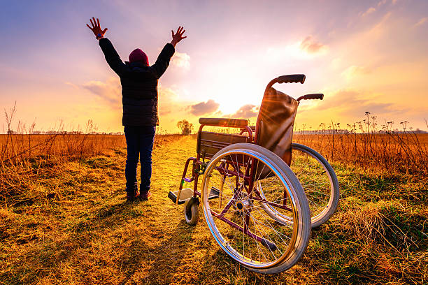 Miracle recovery: young girl gets up from wheelchair and raises Miracle recovery: young girl gets up from wheelchair and raises hands up. Overjoyed young girl  standing up from a wheelchair outdoors. Shot in meadow. Recovery concept miracle stock pictures, royalty-free photos & images