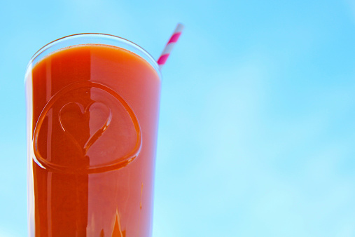 Fresh Carrot, orange and ginger juice against blue sky with stripey paper straw