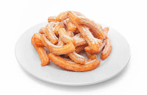 Newly made Spanish churro on white dish isolated on wihte background. Churos is typical pastry mexican breakfast dessert eaten with hot chocolate, lemon cream, sugar and cinnamon, caramel