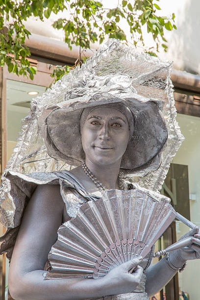 London, United Kingdom - August 6, 2014: A street artist in Covent Garden London. She is dressed as an elegant ladywith an elaborate hat and fan but is completely covered in silver paint.