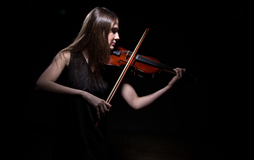 Young woman playing on fiddle on black background