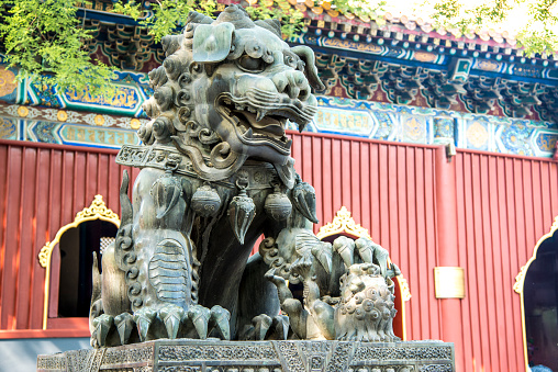 Ancient bronze lion and red chinese pavilliones in Lama Temple (Beijing, China)