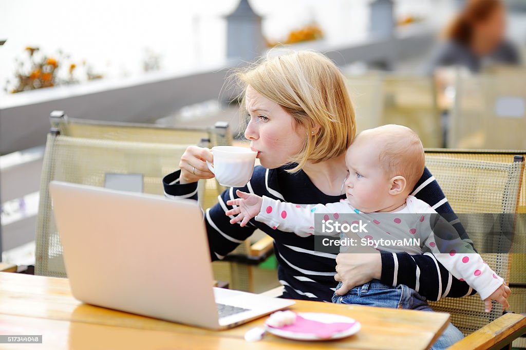 Tired young mother holding 6-month daughter and drinking coffee Tired young mother working oh her laptop, holding daughter and drinking coffee Coffee - Drink Stock Photo