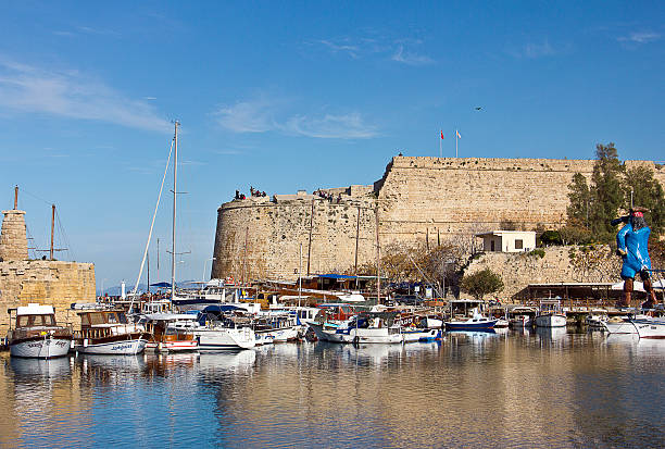 Kyrenia, Cyprus - March 12, 2016: Photo of the waterfront and harbour with sailboats in Kyrenia, Northern Cyprus. People are visiting the harbour for touristic, some of them eating for dinner, some of them are resting near the sea in the Old Harbour in Kyrenia (Girne), Cyprus.