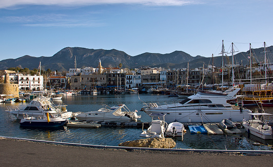 Kyrenia, Cyprus - March 12, 2016: Photo of the waterfront and harbour with sailboats in Kyrenia, Northern Cyprus. People are visiting the harbour for touristic, some of them eating for dinner, some of them are resting near the sea in the Old Harbour in Kyrenia (Girne), Cyprus.