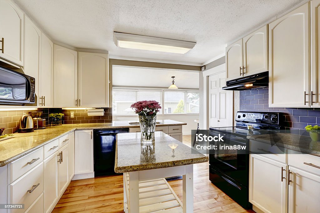 Kitchen room with island and granite tops White kitchen cabinets with black appliances. Kitchen island with granite top decorated with flowers Apartment Stock Photo