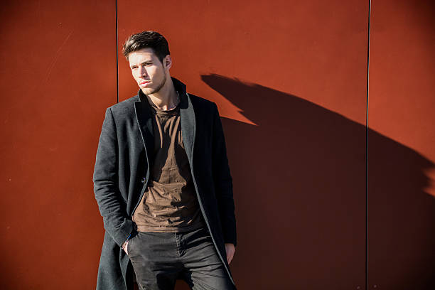 Serious Young Handsome Man in Winter Outfit Leaning on a Red Metal Wall While Looking to a Side of the Frame at Large Copyspace