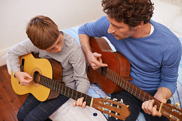 Getting it right together Shot of a father teaching his son the guitar father and son guitar stock pictures, royalty-free photos & images
