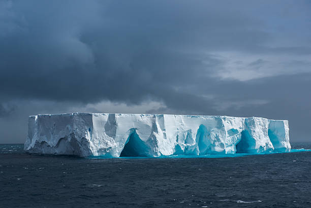 Large tabular iceberg floating in Antarctica Massive flat topped iceberg floating in the Southern Ocean of Antarctica showing the weathered cracks, fissures holes and caves on the sides antarctica travel stock pictures, royalty-free photos & images