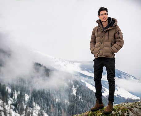 Handsome man in outerwear sitting while looking at camera. Snowy landscape on background