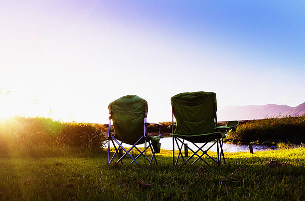zwei campingplätze stühlen von sonnenbeschienenen fluss in der abenddämmerung zu genießen. idyllische. - campingstuhl stock-fotos und bilder