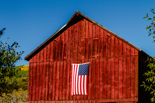 American flag hanging on side of rustic red barn on sunny autumn afternoon