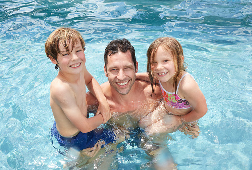 Portrait of a father and his two young children in a swimming pool