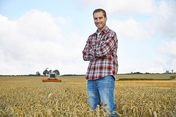 istock Farmer stands in field with combine harvester behind 517403107