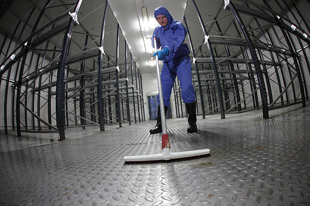 worker in uniform cleaning floor in empty storehouse stock photo