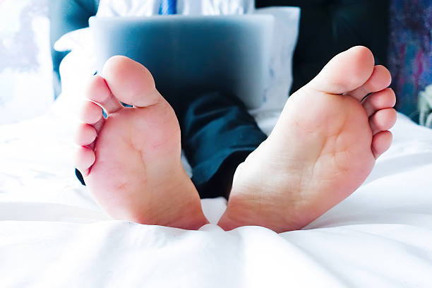 бизнесмен лежал на кровати, с помощью ноутбука в номере - professional occupation human foot clothing concentration стоковые фото и изображения