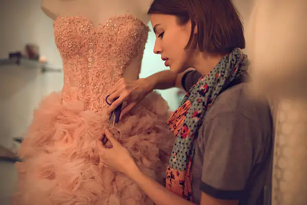 Photo of Clothing designer cutting material on a dress in workshop.