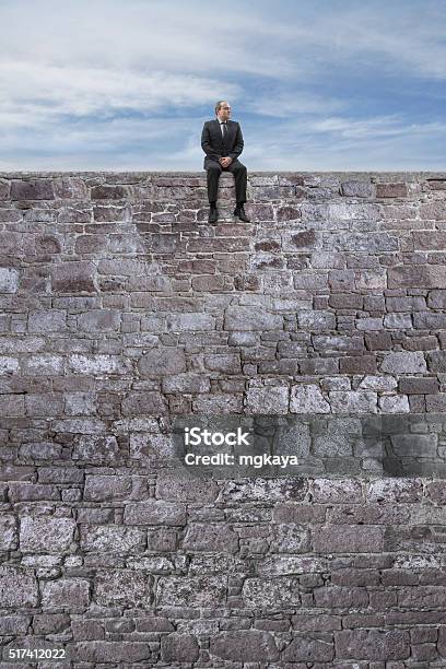 Businessman Sitting On Wall With Legs Hanging Stock Photo - Download Image Now - Adult, Ancient, Aspirations