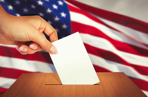 Hand putting a ballot into ballot box with american flag behind