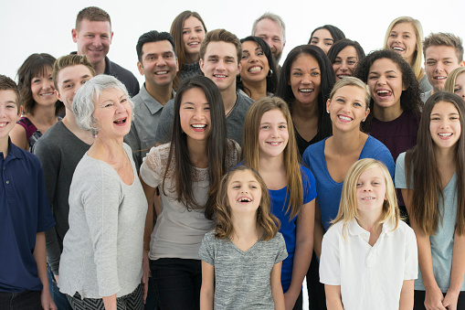 A multi-ethnic group of multi-generational families are standing together in a large group and are laughing and smiling.