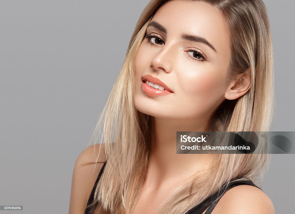 Beautiful young woman smiling posing on gray background Beautiful young woman portrait smiling posing attractive blond with flying hair on gray background. Studio shot. Women Stock Photo