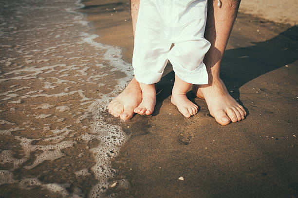 father and baby feet walking on sand beach