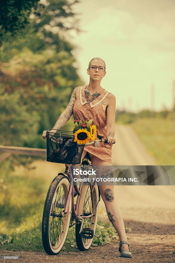 Blonde woman with cruiser bicycle Young blonde woman (with tattoos on her arms and legs) posing on a deserted country road with her vintage cruiser style bicycle. Cycling Stock Photo