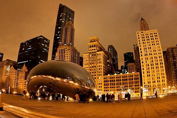 Cloud Gate at Night Chicago, United States - December 23, 2012: The steel sculpture named Cloud Gate in Millennium Park in Downtown Chicago at night. It is surrounded by some curious people looking and taking pictures of it and their reflections. The Cloud Gate, also called The Bean, was created by Indian-born British artist Anish Kapoor. millennium park stock pictures, royalty-free photos & images