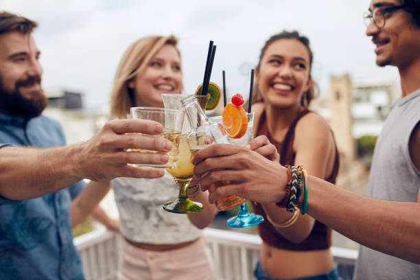 Friends toasting cocktails at a party Friends having fun and drinking cocktails outdoor on a rooftop get together. Group of friends hanging out and toasting drinks outdoors. Focus on glasses. cocktail party stock pictures, royalty-free photos & images