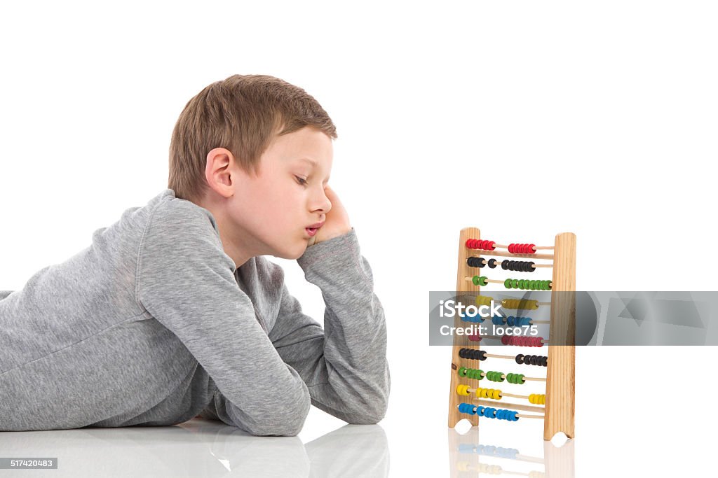 Boring maths Bored schoolboy lying on the floor and looking at colorful abacus. Waist up studio shot isolated on white. 10-11 Years Stock Photo