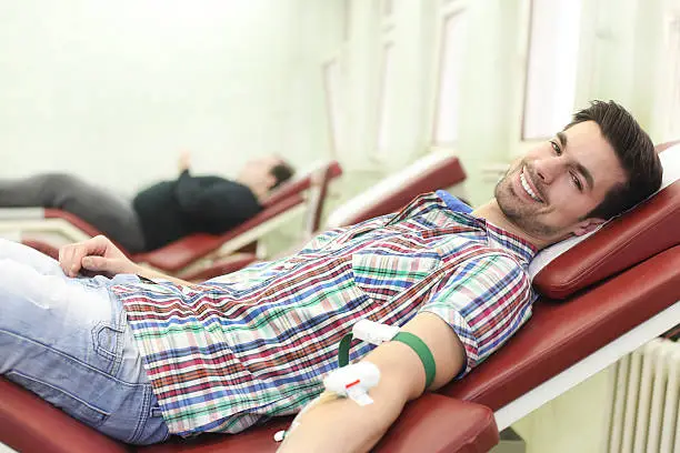 People lying in a hospital giving a blood donation. Group of patients in row, selective focus on the smiling young Caucasian brunette.