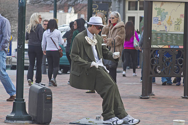 Leaning Living Statue Asheville, North Carolina, USA - March 2, 2014: Living statue street artist showing a man in a suit being blown backward and leaning at an impossible angle surrounded by people on the street going about their business on March 2, 2014 in downtown Asheville, NC person falling backwards stock pictures, royalty-free photos & images