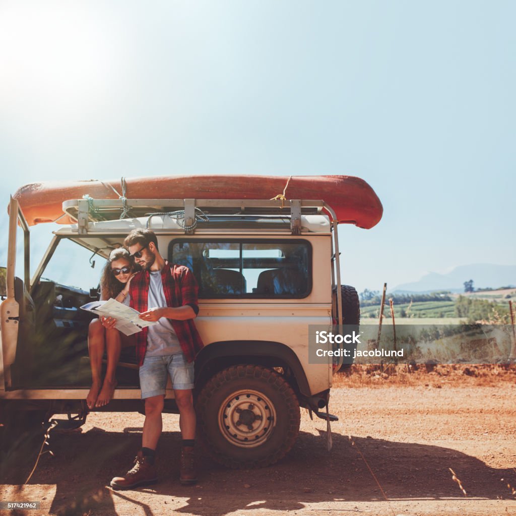 Couple taking a break to look at map on roadtrip Young couple stopping on country road and looking at the map for directions. Man and woman on a road trip in countryside on a summer day. Road Trip Stock Photo