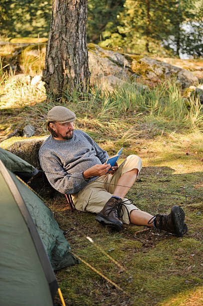 istock Senior man sits outside a tent and reads a book 517423075