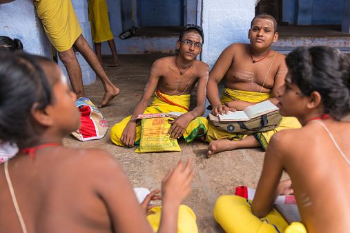 Madurai, India - December 26, 2013. Four young boys in yellow dress sitting on the floor with their books and debating about what they learn.