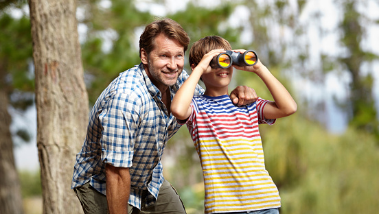 Shot of a young boy looking through binoculars while with his father in the outdoors