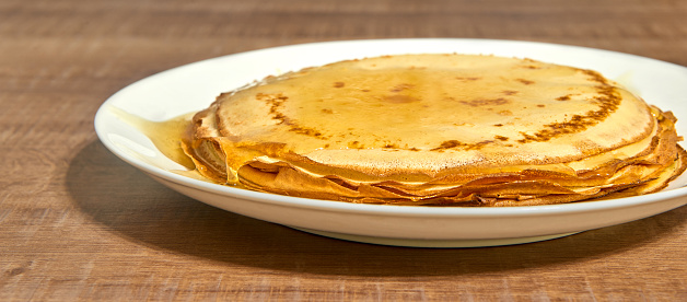 Pancakes with honey on white plate and wooden table