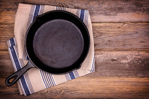 Empty skillet Empty cast iron skillet with tea towel, over old wood background. Retro style processing and space for your text. skillet cooking pan photos stock pictures, royalty-free photos & images