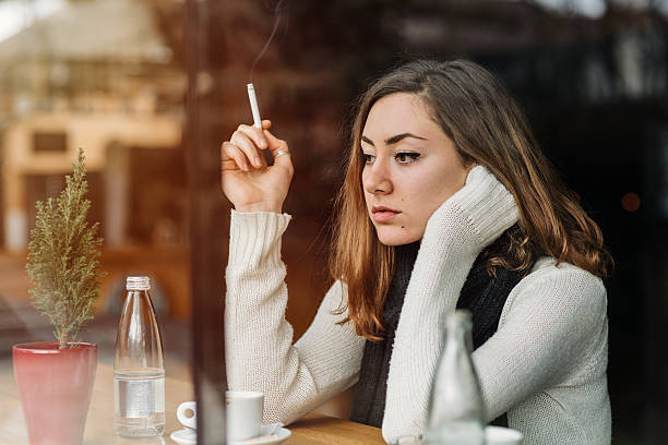 Young girl smoking and feeling depressed in a bar. Reflections from the window.