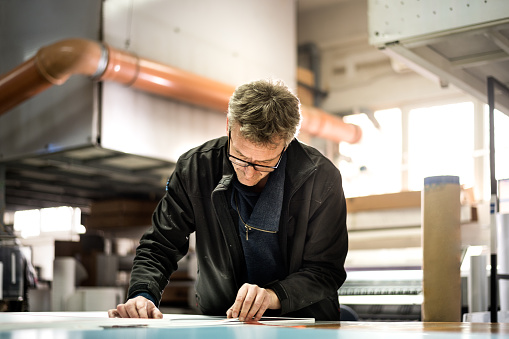 Skilled worker with eyeglasses inside the printing factory working on prepress materials.