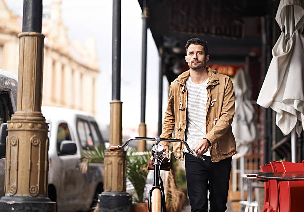 Cropped shot of a young man pushing his bicycle through the city