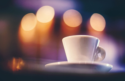Closeup of a cup of espresso coffee in under vibrant glimmering lights, Low angle shot.