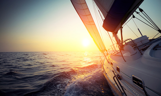 Sail boat gliding in open sea at sunset